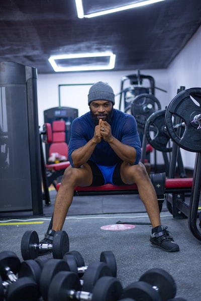 身穿蓝色背心和蓝色短裤的男子坐在黑色和红色的运动器材上